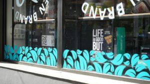 A person applying large, colorful vinyl graphics to a street-facing window of a small storefront.
