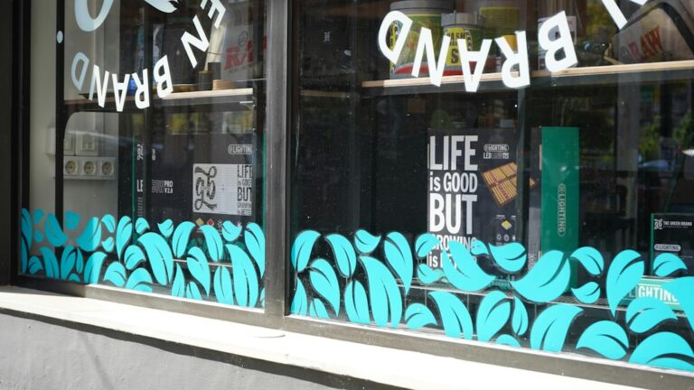 A person applying large, colorful vinyl graphics to a street-facing window of a small storefront.